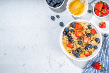 Summer morning oatmeal with berry. Homemade healthy breakfast oats with strawberry, blueberry, honey, nuts and mint on white marble background