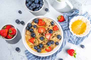 Summer morning oatmeal with berry. Homemade healthy breakfast oats with strawberry, blueberry, honey, nuts and mint on white marble background