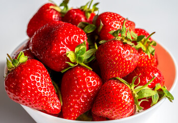 Ripe juicy strawberries in a white cup on a white background