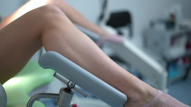 Close-up side view slim female Caucasian legs spread on gynecological chair. Unrecognizable young woman consulting gynecologist waiting for doctor in hospital indoors