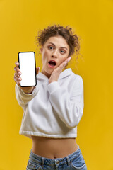Naklejka premium Concerned blurred woman showing switched on screen phone indoor. Close up view of smartphone with blank white screen, holding by excited girl, isolated on orange studio background. Concept of device.