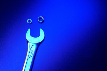 Two metal nuts and a spanner which creates a small funny smile face. Metal composition on the black table in a blue light. Space for text. Background picture.