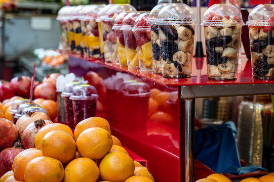 Fruits are harvested and stacked on the counter in the market for squeezing juice on a manual press. Assorted fruit pieces in a transparent glass. Close-up.