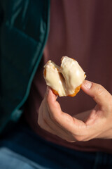 A man's hand holds a bitten donut, a sweet snack with donuts and takeaway coffee on a park bench,...