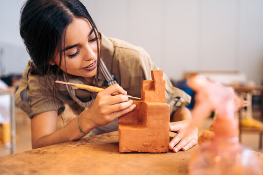 Young craftswoman carving geometric shape from clay