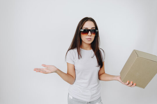 Girl Standing against White Background in Basic T-Shirt and Sunglasses Holding Cardboard Box