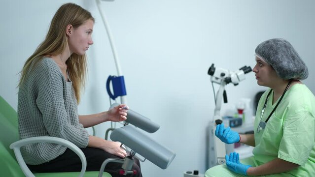 Side view thoughtful sad teenage girl with positive pregnancy test sitting on gynecological chair with doctor persuading on abortion. Problem of adolescent pregnancy and health care