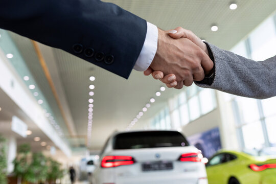 handshake close-up on the background of a car dealership, the concept of a successful purchase of a new car on credit