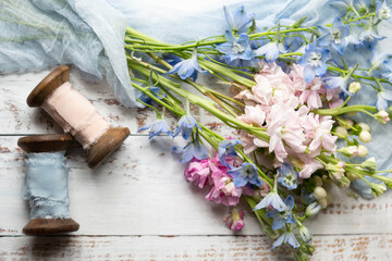 Top View of Bouquet of Blue Bellflowers, Pink Stock and Hypericum Berries on a White Wooden Table with Wooden Spools of Pink and Blue Silk Flowers