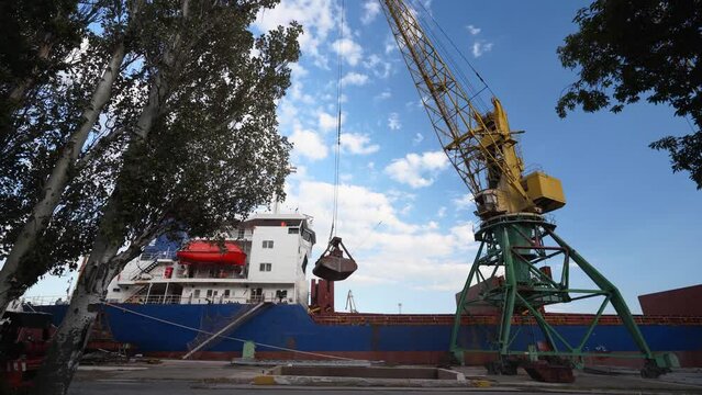 Grain transshipment from container to ship cargo holds with a double rope dual scoop clamshell grab on crane in sea port. Wheat shipment with water transport. Agricultural commodities transportation.
