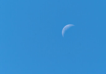 Peaceful view of the moon over a clear blue sky.	