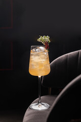 Light yellow alcoholic cocktail in a thin glass, decorated with gypsophila flowers on a dark bar background