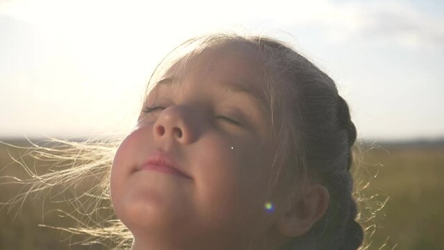 Happy child. cute free girl dreams with her eyes closed. Close-up portrait of child in rays of the sun outdoors. Emotions of freedom of girl dreaming with closed eyes. Childhood freedom concept