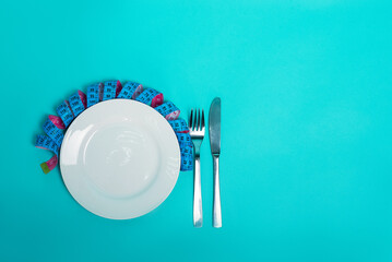 Healthy eating weight loss fitness. Empty plate with fork knife measuring tape in centimeters on a blue background from above. Diet menu Obesity. Place for an inscription. Advertising. - 511120364