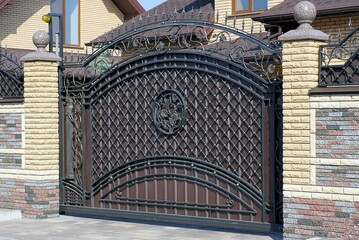 one large brown metal gate with a black wrought iron pattern on a brick wall of a fence on a gray...