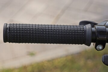 one black plastic grip on the handlebars of a sports bike outdoors on a gray background