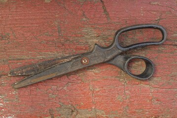 one black metal old rusty scissors lies on a red wooden shabby table