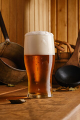 Glass of lager beer, wooden bucket and ladle in the interior of the sauna. Mug of light beer and bath accessories are in the interior of the Russian bath.  Shallow depth of field.