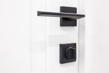 Fototapeta na wymiar Modern black door handle on white wooden door in interior. Knob close-up elements. Door handle, fittings for interior design