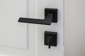 Modern black door handle on white wooden door in interior. Knob close-up elements. Door handle, fittings for interior design