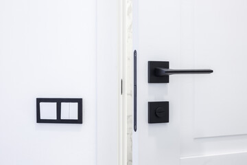 Modern black door handle on white wooden door in interior. Knob close-up elements. Door handle,...