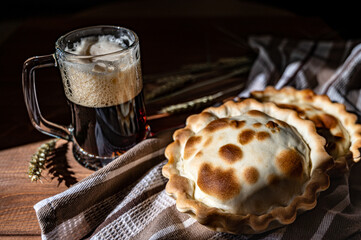Close-up several meat pies and a glass of dark beer stand modestly on the table. © Marina Gordejeva