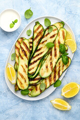 Grilled zucchini slices in a white plate on a blue background. Healthy summer veggie food. Top view