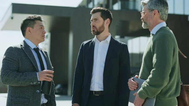 Footage of multicultural group of three good-looking men talking to each others near office during lunch break. Asian and Caucasian ethnicity. Business people concept. Share ideas. Outdoor