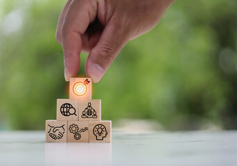 Concept of business strategy and action plan. Hand putting wooden cube block stacking with icon on green background