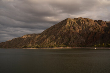 The desert, rocky mountains and placid lake under a cloudy sky, at sunset. 