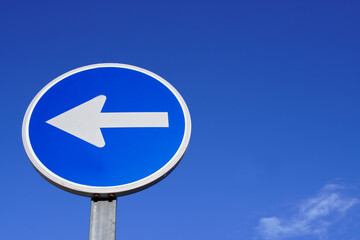 round traffic sign with arrow over blue sky