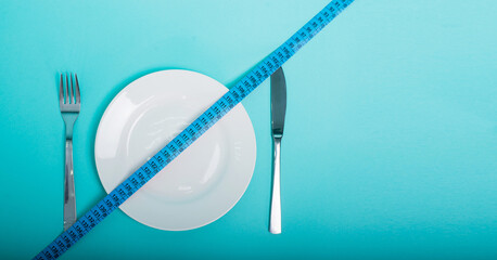 Healthy food, fitness for weight loss. An empty plate, fork and knife with a measuring tape in centimeters on a blue background from above. Diet menu Obesity Place for an inscription Advertising - 511130119