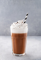 Hot chocolate with whipped cream in a tall glass on a blue background. Front view and copy space
