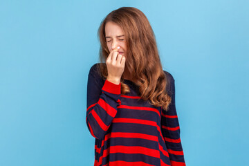 Stink, awful odor. Woman wearing sweater pinching nose, stop breathing bad odor, disgusted by smell of farting, her grimace expressing repulsion, gross. Indoor studio shot isolated on blue background.