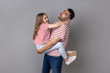 Portrait of funny father and smiling charming daughter in striped T-shirts standing together, tired...