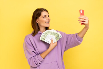 Portrait of smiling woman with dark hair making selfie with big fan of euro banknotes, showing...