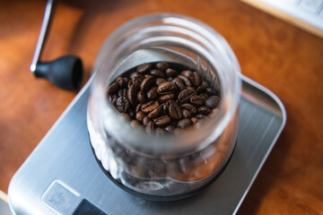 Coffee beans in a glass jar on an electronic scale, with a manual coffee grinder beside.