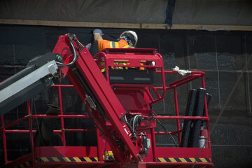 Fototapeta premium worker installing a self-adhering waterproofing membrane on below-grade concrete walls foundation