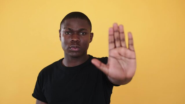 Stop racism. Black man showing blocking gesture. Racial discrimination blockage. Serious rejecting man showing refusal hand sign isolated on orange background.