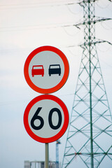 No overtaking and speed limit signs against industrial sky.