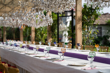 Crystal and glass goblets and glasses, white plates, cutlery for festive table setting for luxurious wedding or birthday party. Soft focus. 