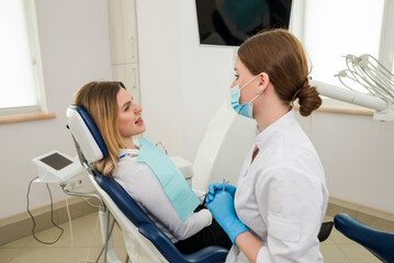 A beautiful female dentist is talking to a patient while sitting in a chair.