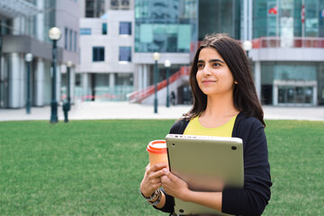 Happy young girl student walking with laptop computer and cup of coffee on campus