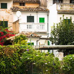 Fototapeta na wymiar Facades of white buildings with green shutters for windows surrounded by flowers and greenery, Spain, Mallorca.