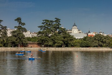 People in rowboats on the lake of the Madrid country house, on a summer day and with a view of the Almudena Cathedral                       