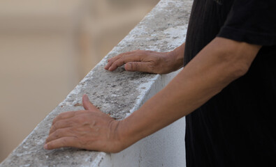 Hands of an unidentified senior male on cement railing