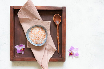 Himalaya pink salt with orchid flower on the wooden tray on white marble background top view. Spa and wellness concept.