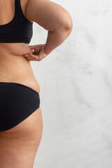 Cropped rearview of fat, adipose, overweight female body in black underwear, checking and holding...