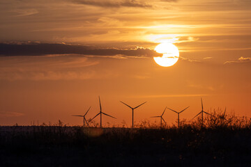 Many windmills in distance on large field against backdrop of rising sun on orange background with...