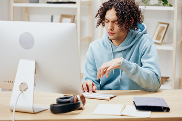A young man sitting in front of the computer work at home interior